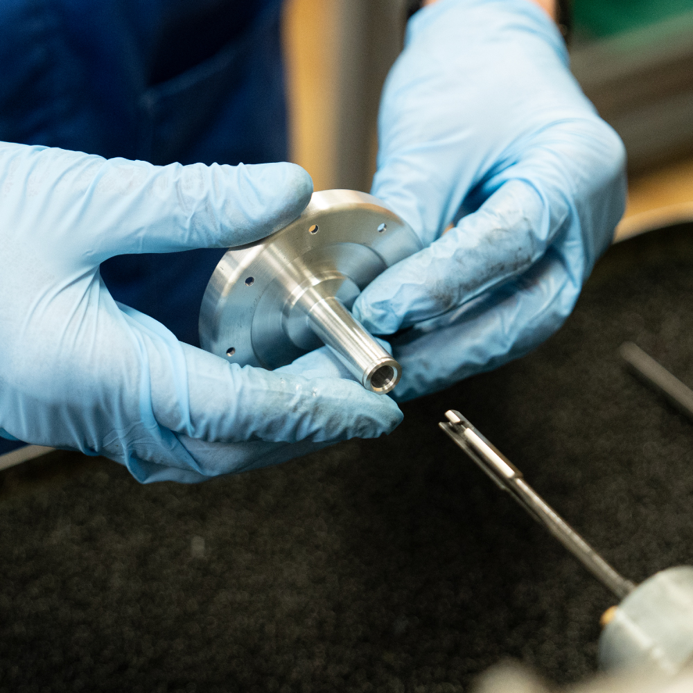 Close up of 2 hands wearing blue gloves holding precision engineering part